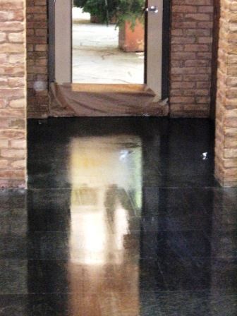 Black, reflective tiled floor leading to a glass door with brick columns on either side.