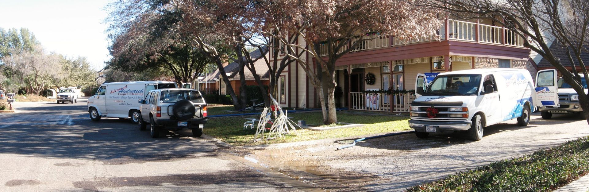 Several vans and a Jeep parked on a street in front of a two-story building with a porch and red awning.