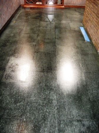 Dark tiled floor with bright reflections near a wooden door and wall.