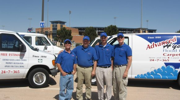 Four men in blue shirts pose by company vans, 