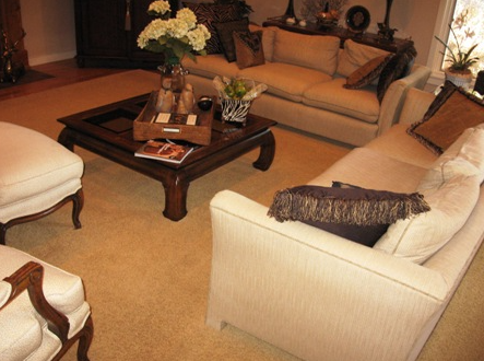 Living room with beige sofas, patterned pillows, dark wood coffee table, and light carpet.