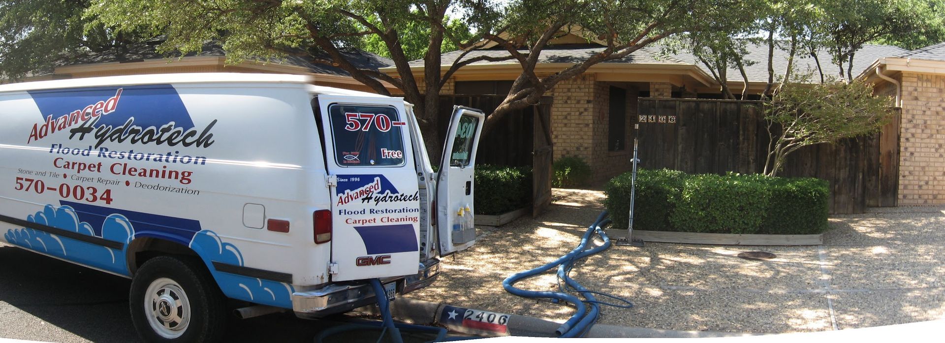 A white carpet cleaning van parked in front of a house with blue hoses connected to the front door.