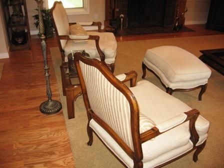Two antique chairs with a matching ottoman, light-colored upholstery, set in a room with wood floors and a fireplace.