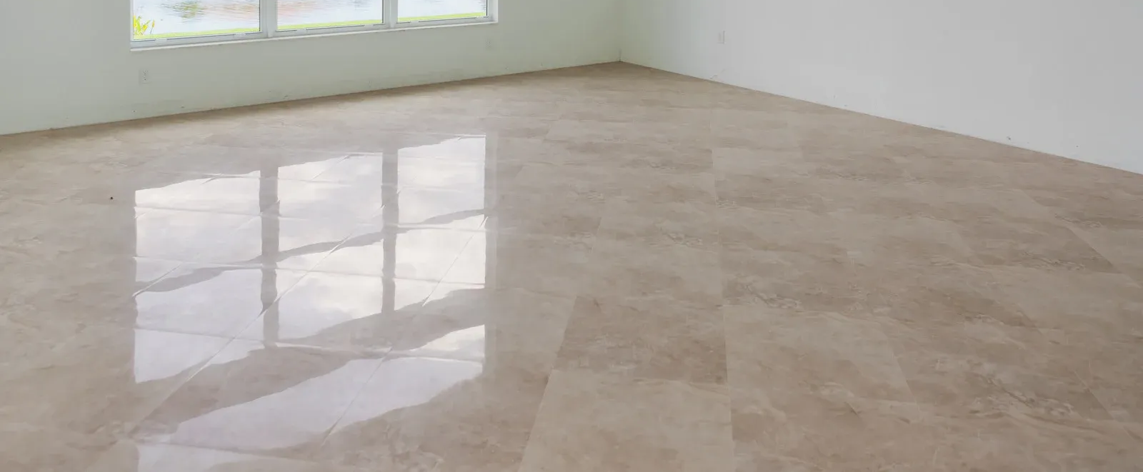 Shiny beige tiled floor reflecting a window, in an empty room with white walls.