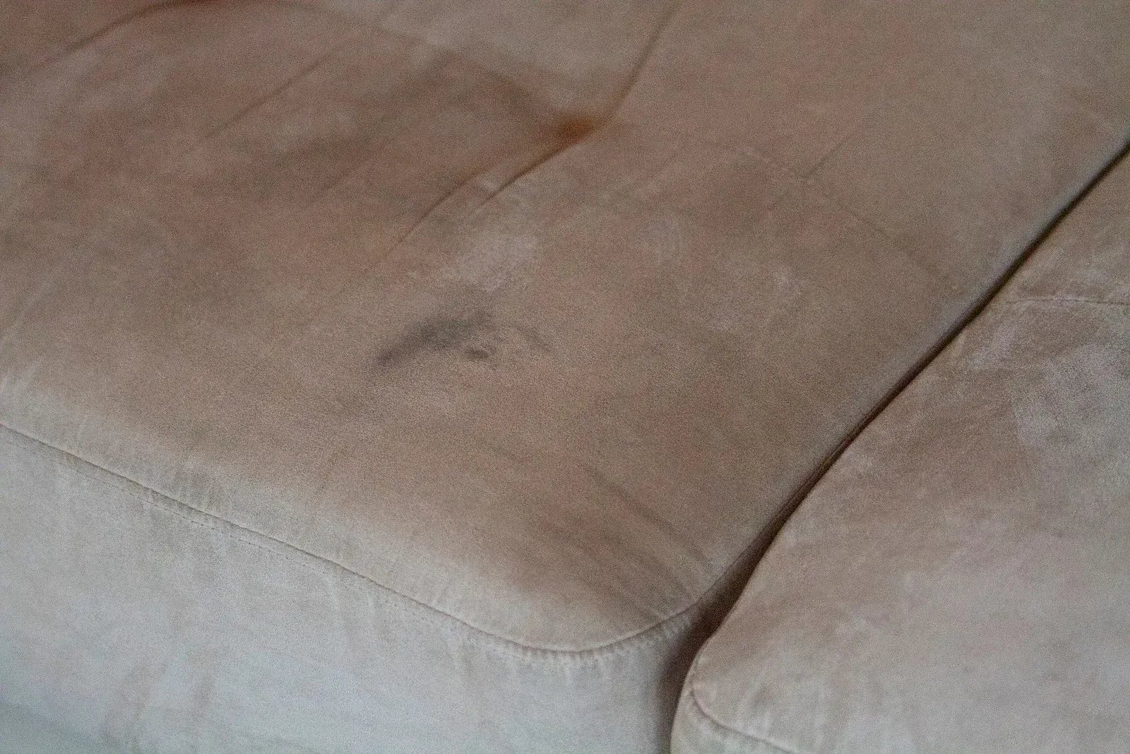 Close-up of a beige fabric couch cushion with a dark stain.
