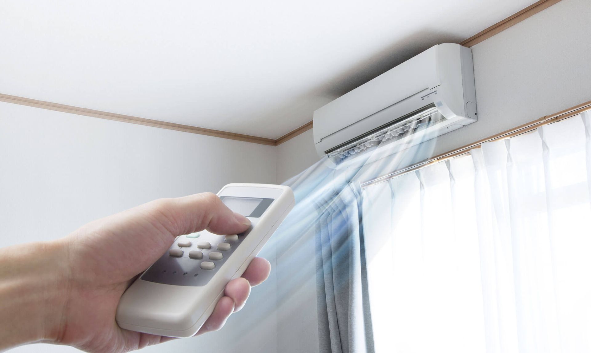 Mano sosteniendo un control remoto apuntando a un acondicionador de aire montado en la pared que sopla aire frío.