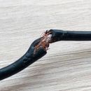 Cable eléctrico negro dañado con cables de cobre expuestos y aislamiento quemado.