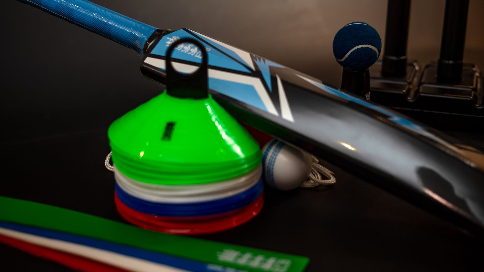 A cricket bat is sitting on a table next to a stack of cones and a tennis ball.