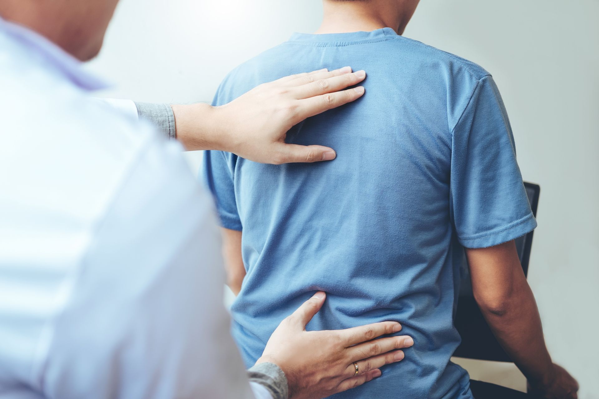 A man is sitting in a chair while a doctor examines his back.