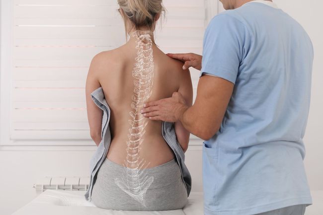 A man is examining a woman 's back with a diagram of the spine.