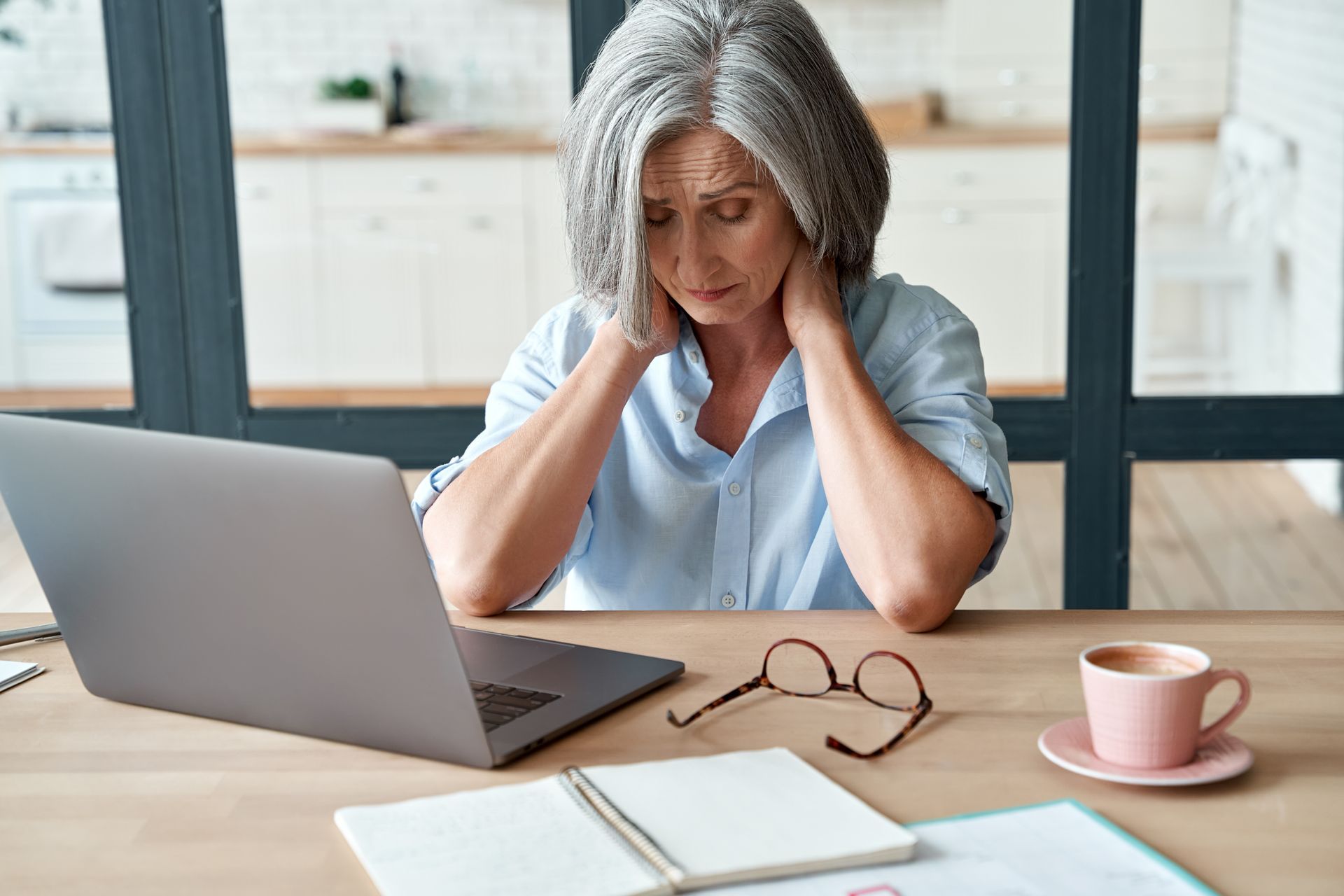 An older woman is sitting at a table using a laptop computer.