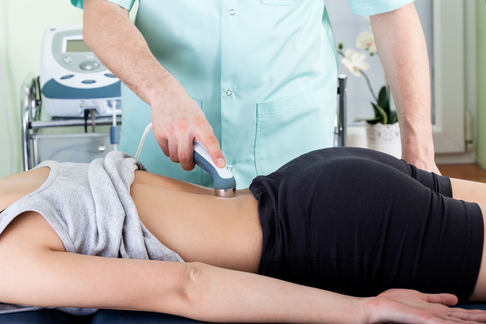 A woman is laying on a bed getting a laser treatment from a doctor.