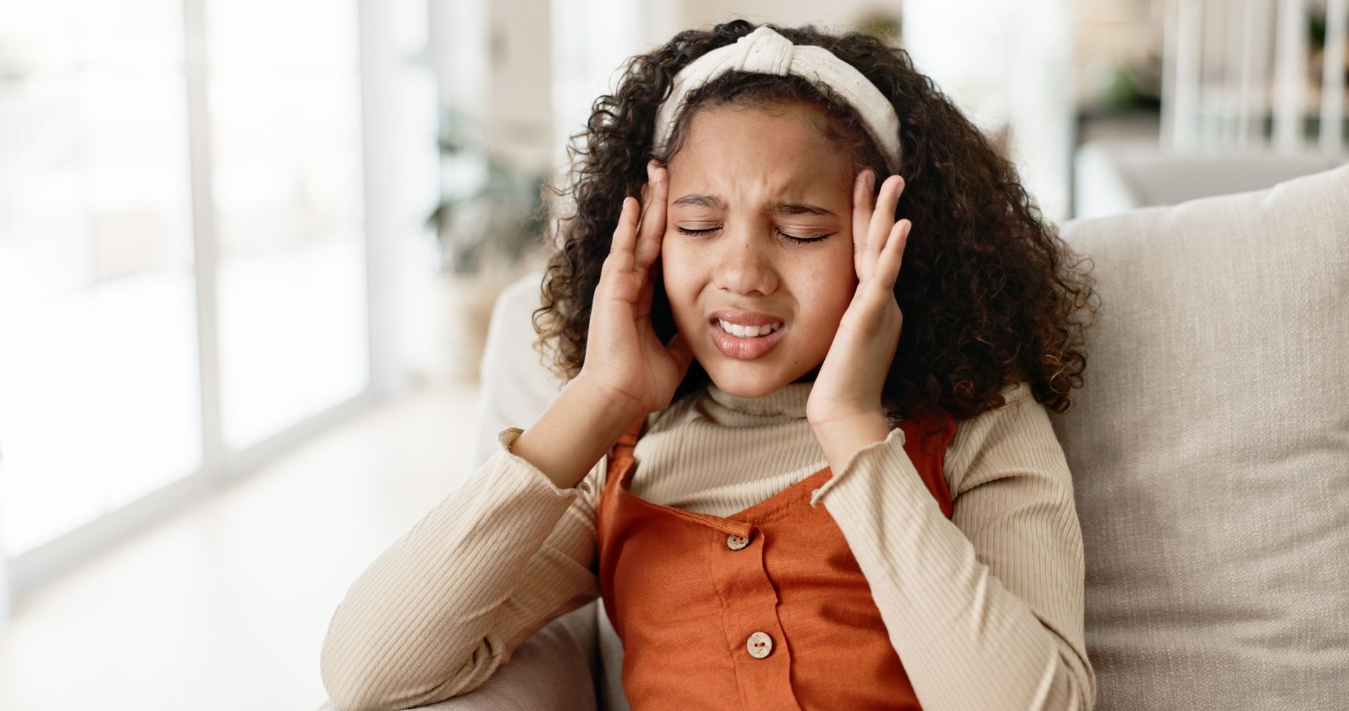 A young girl is sitting on a couch with a headache.