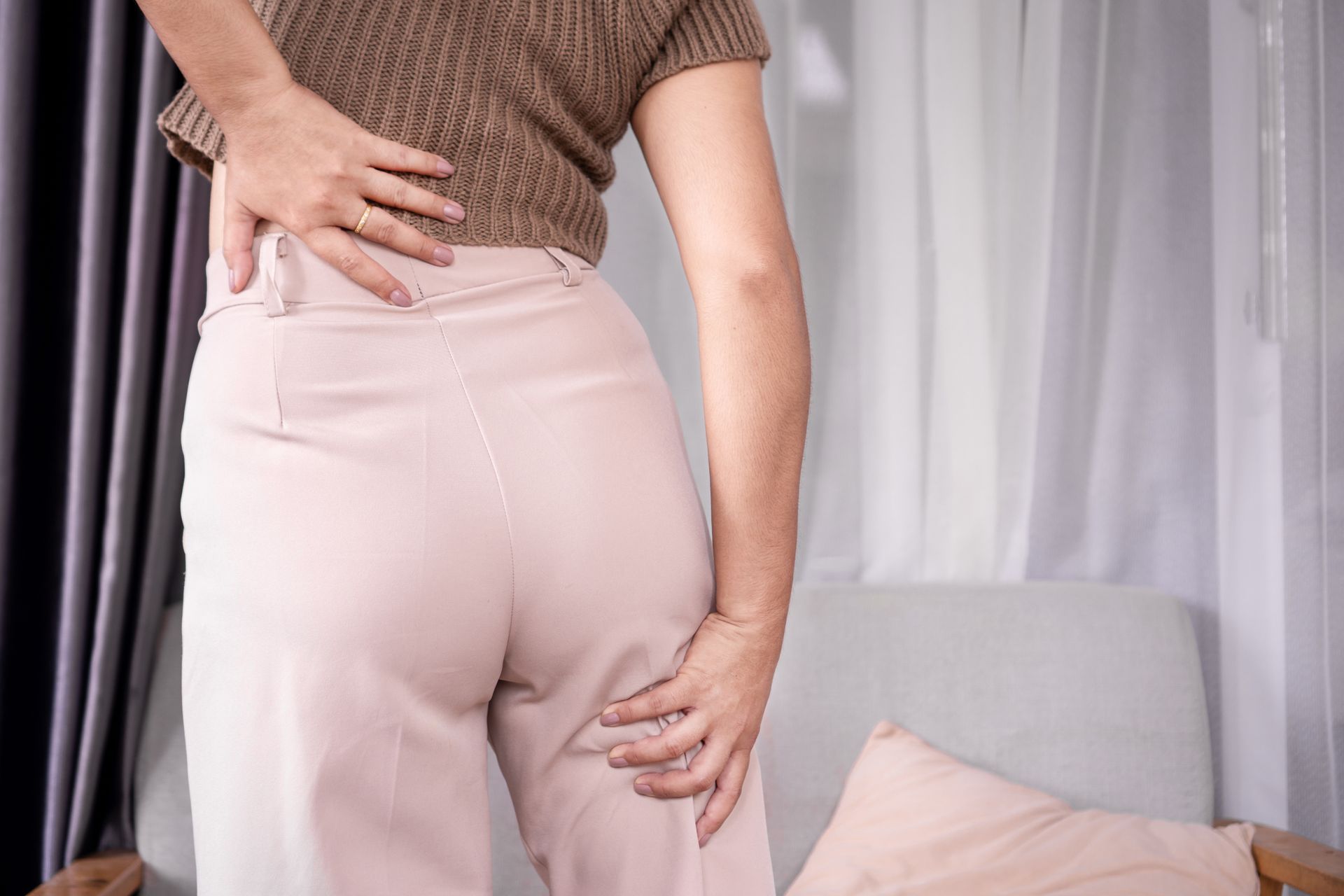 A woman is holding her back in pain while sitting on a couch.