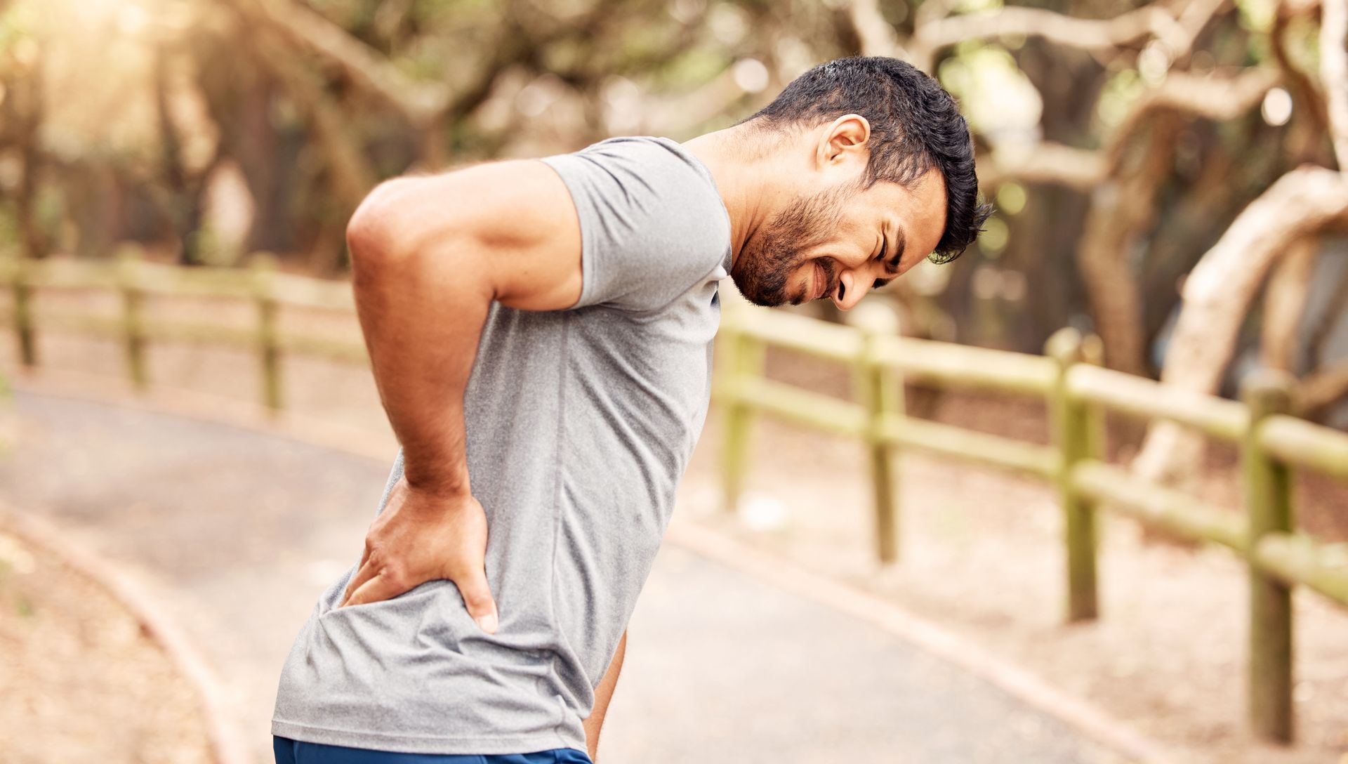 A man is holding his back in pain while standing on a path.