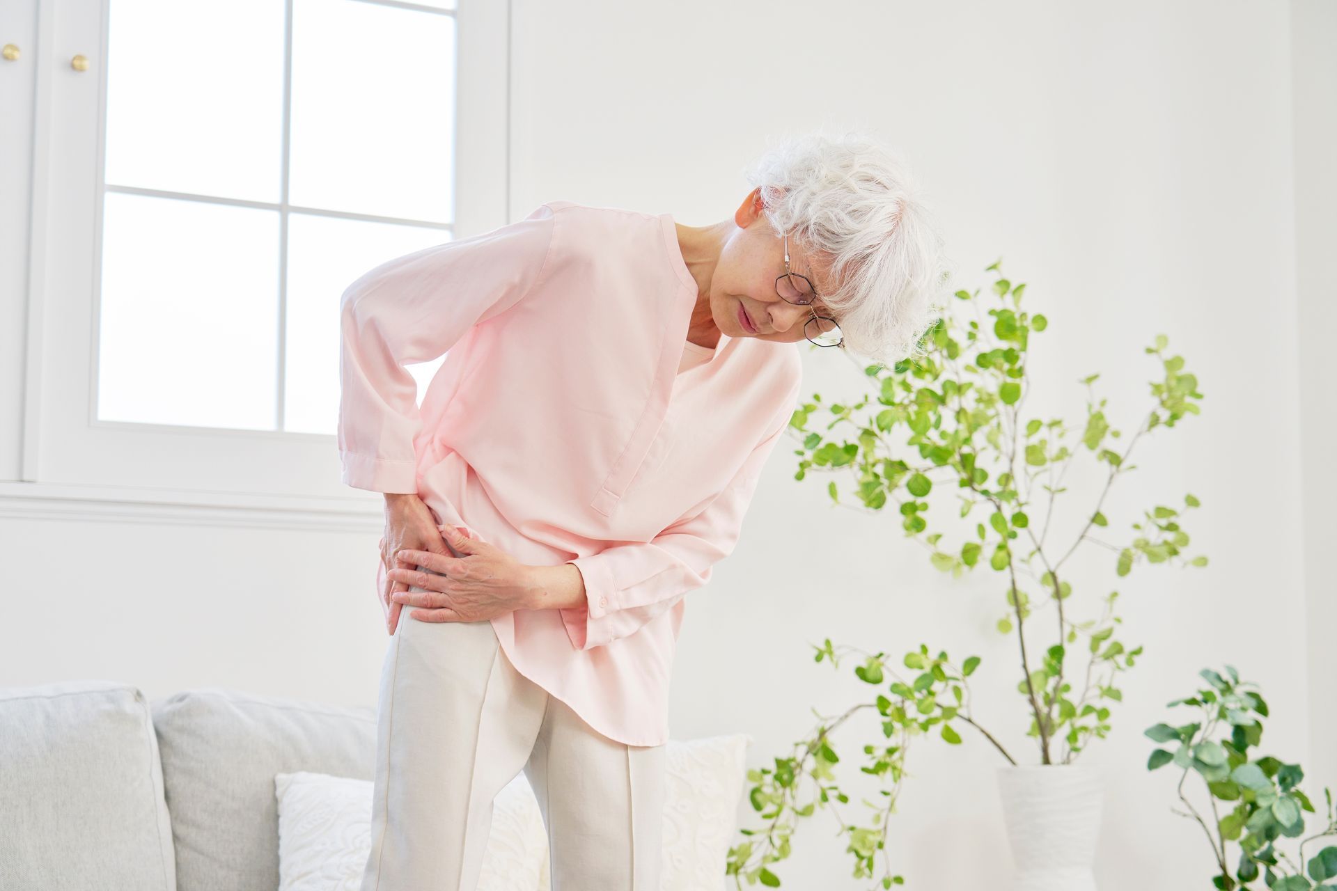 An elderly woman is holding her knee in pain in a living room.