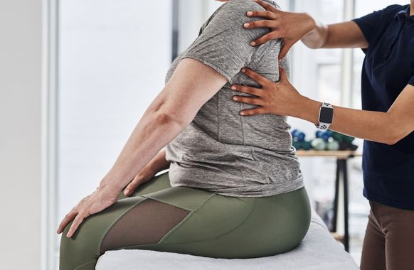 A woman is sitting on a table getting a massage from a doctor.