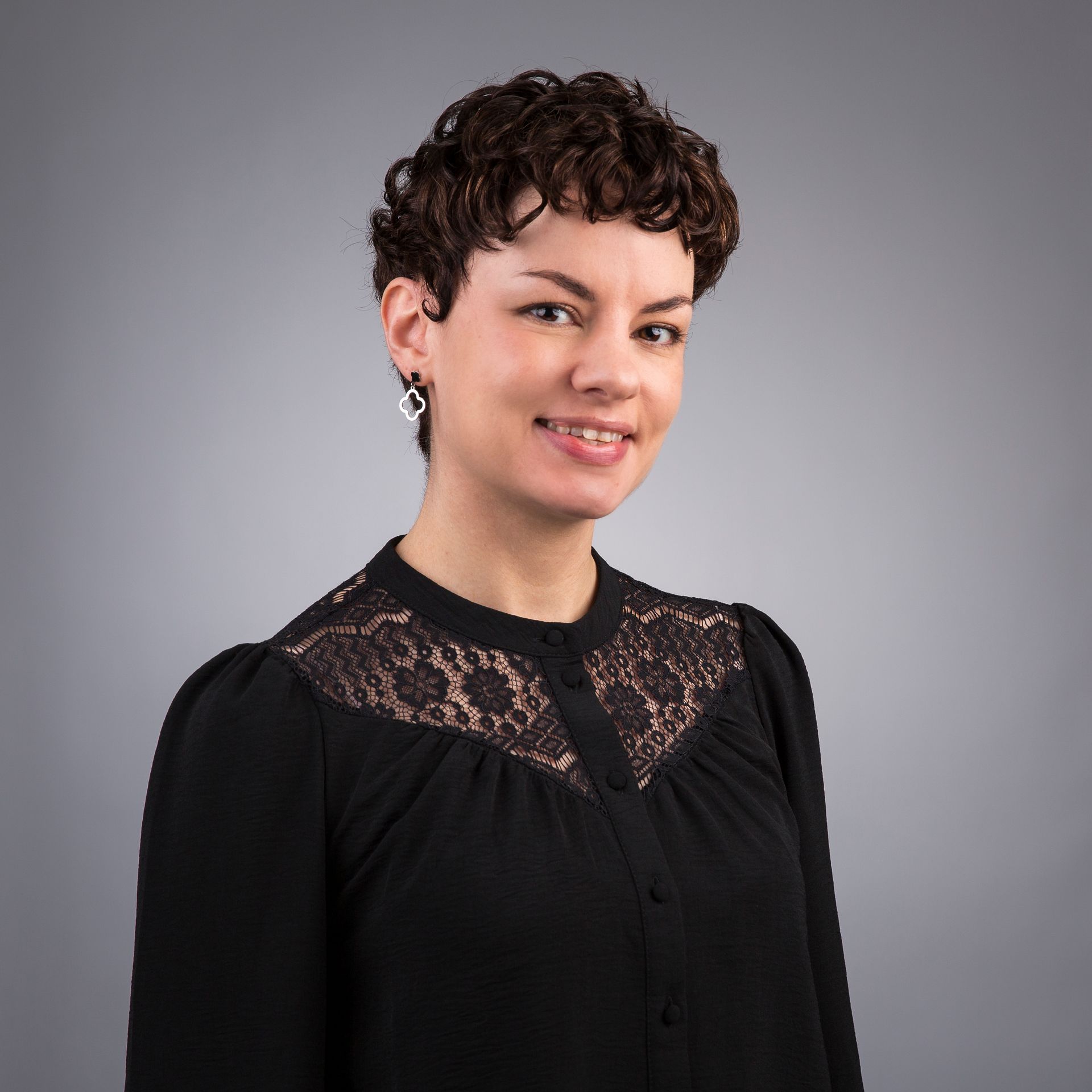 Een vrouw met krullend haar draagt een roze jasje en lacht.