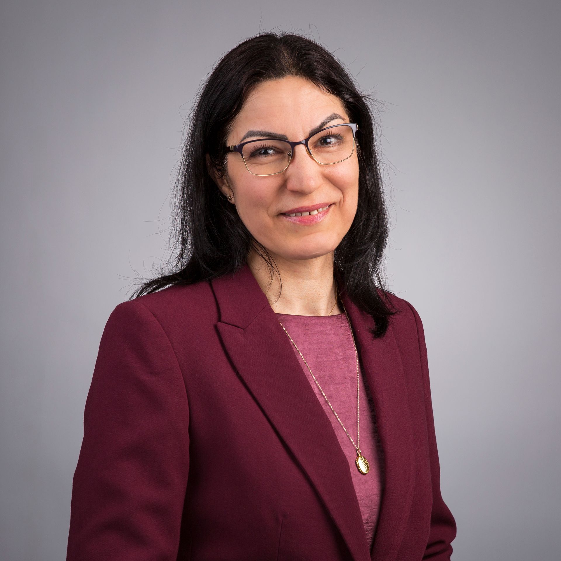 Een vrouw met een bril en een roze shirt lacht naar de camera.