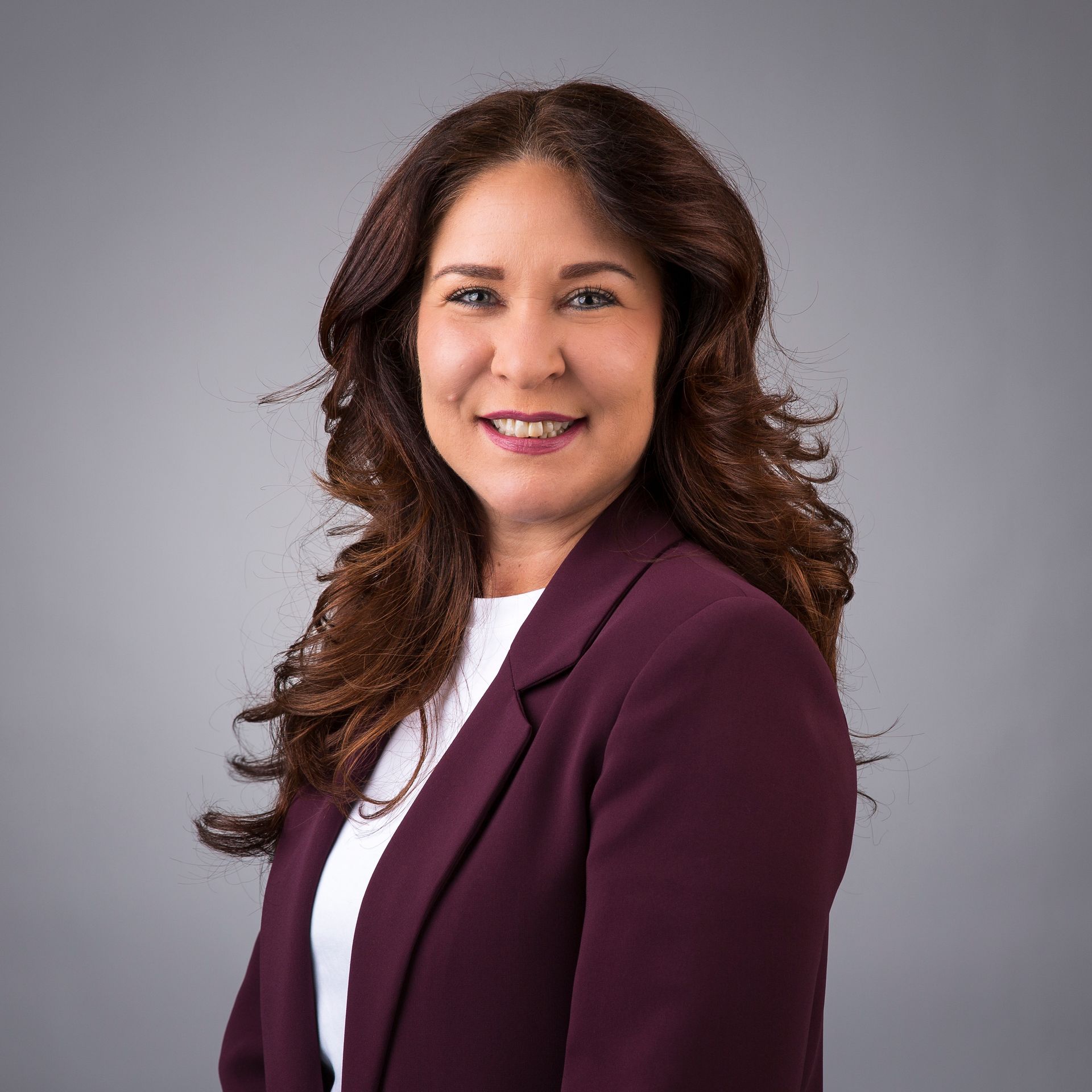 Een vrouw met lang bruin haar draagt een zwarte trui en lacht.