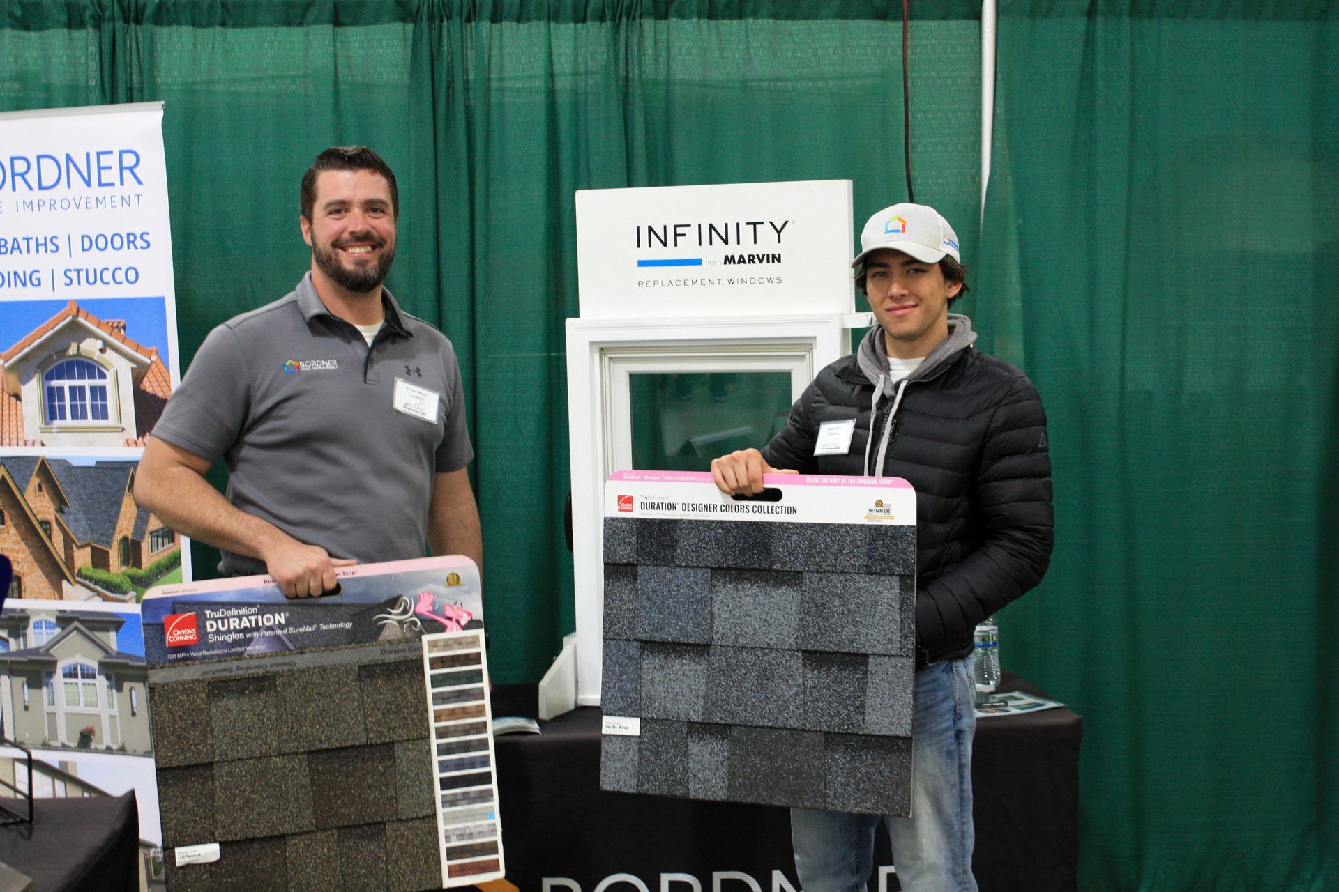 Two men are standing next to each other in front of a sign that says infinity