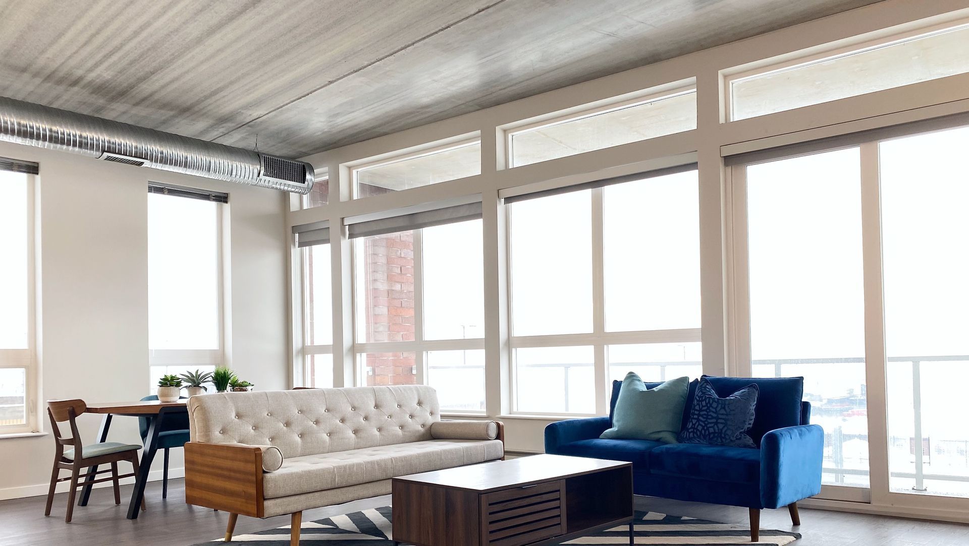 A living room with a couch , chair , table and lots of windows.