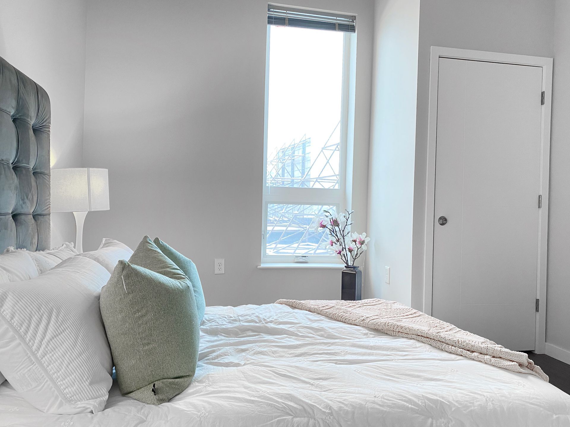 A bedroom with a bed , window , lamp and door.