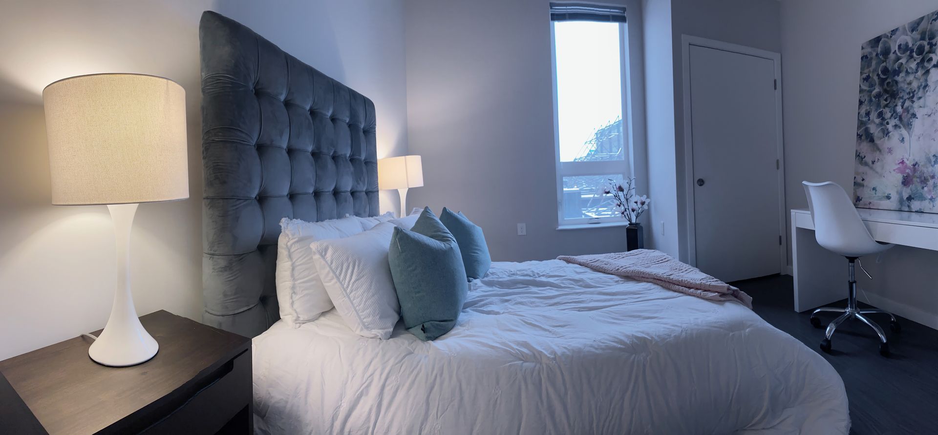 A bedroom with a bed , nightstand , lamp and desk.
