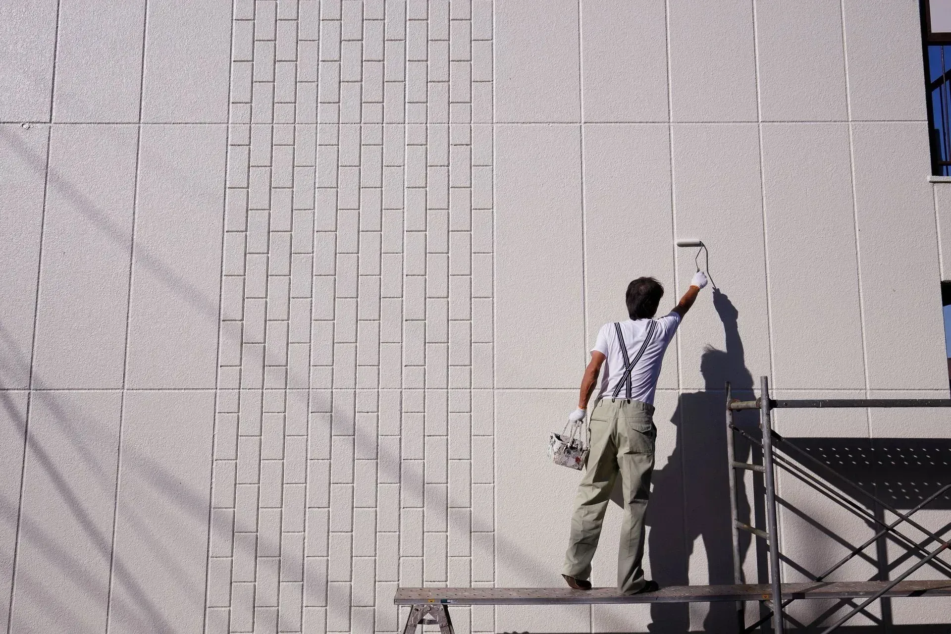A man is standing on a scaffolding painting a wall.