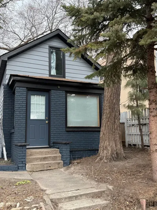 A small blue brick house with a tree in front of it.