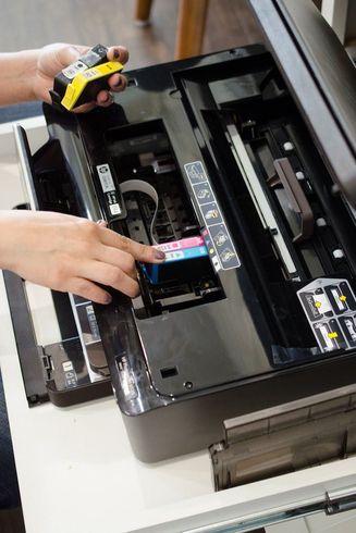 A person is fixing a printer with a yellow tape measure.