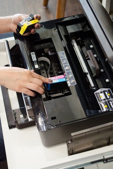A person is fixing a printer with a yellow tape measure.