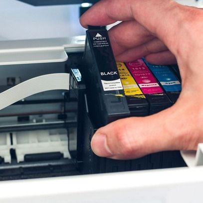 A person is putting a black ink cartridge into a printer
