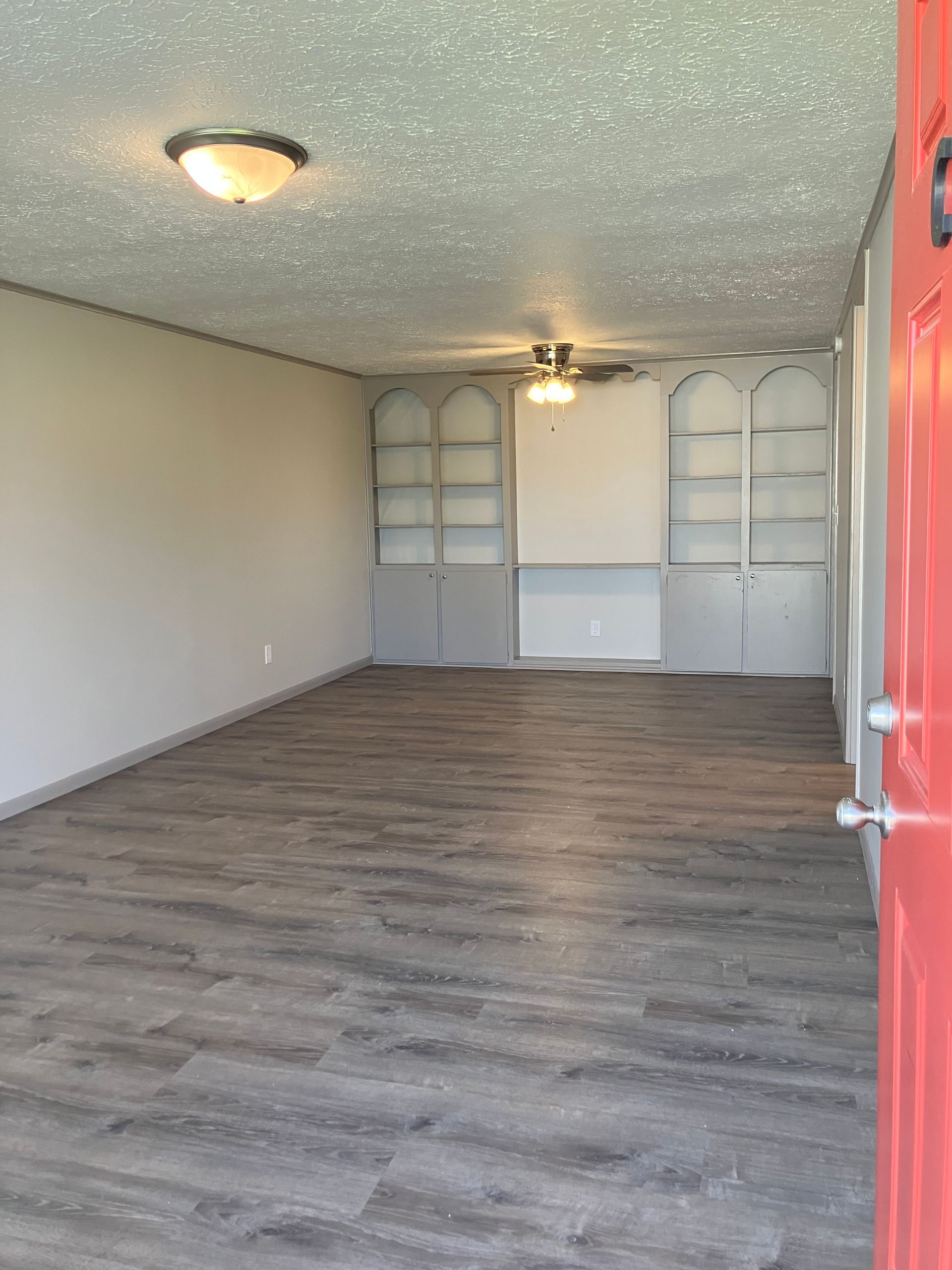 An empty living room with hardwood floors and a red door.