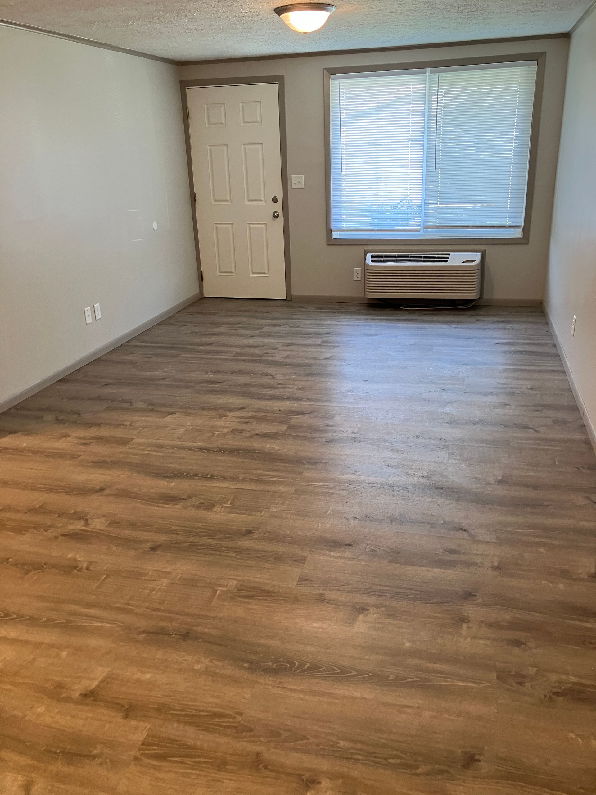 An empty living room with hardwood floors and a window.