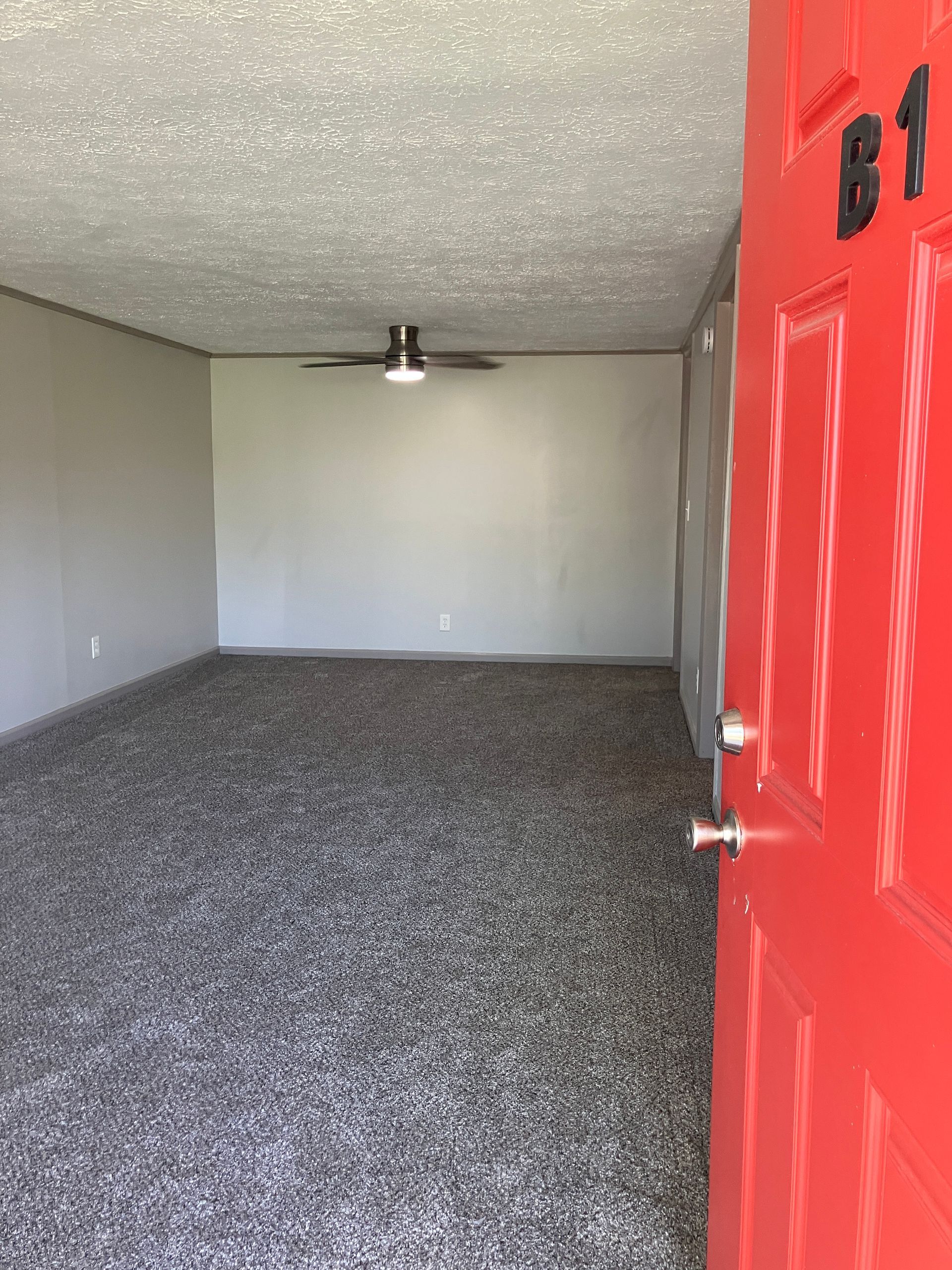 An empty living room with hardwood floors and a red door.
