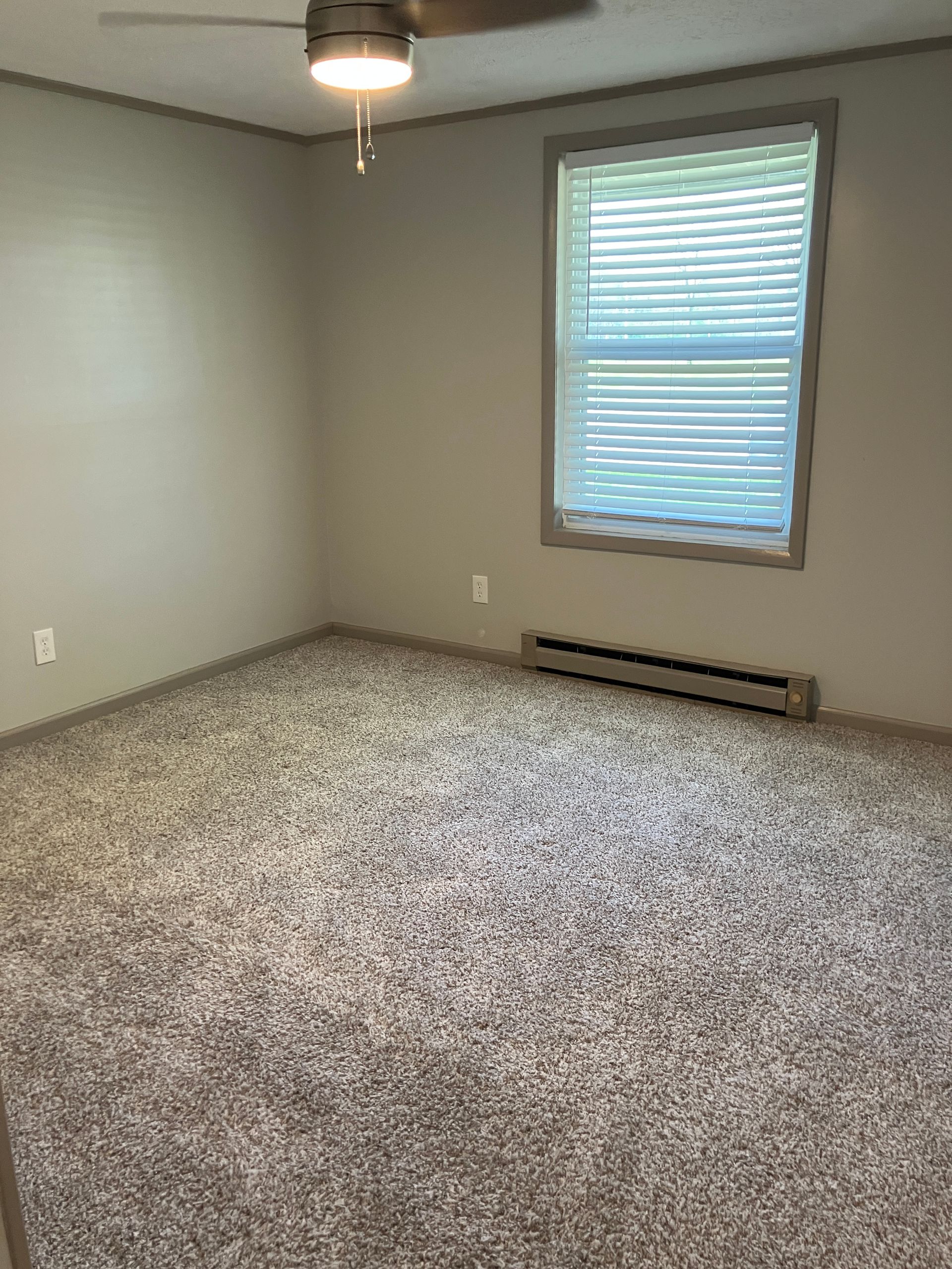 An empty bedroom with a ceiling fan and a window.