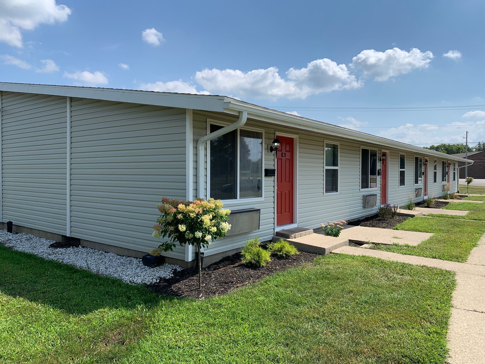 A white house with a red door and windows is sitting on top of a lush green lawn.