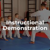 A group of children are practicing karate with a teacher in a gym.