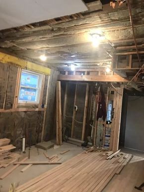 Dim room under renovation with exposed framing, bare ceiling, stacked lumber, and a lit window.
