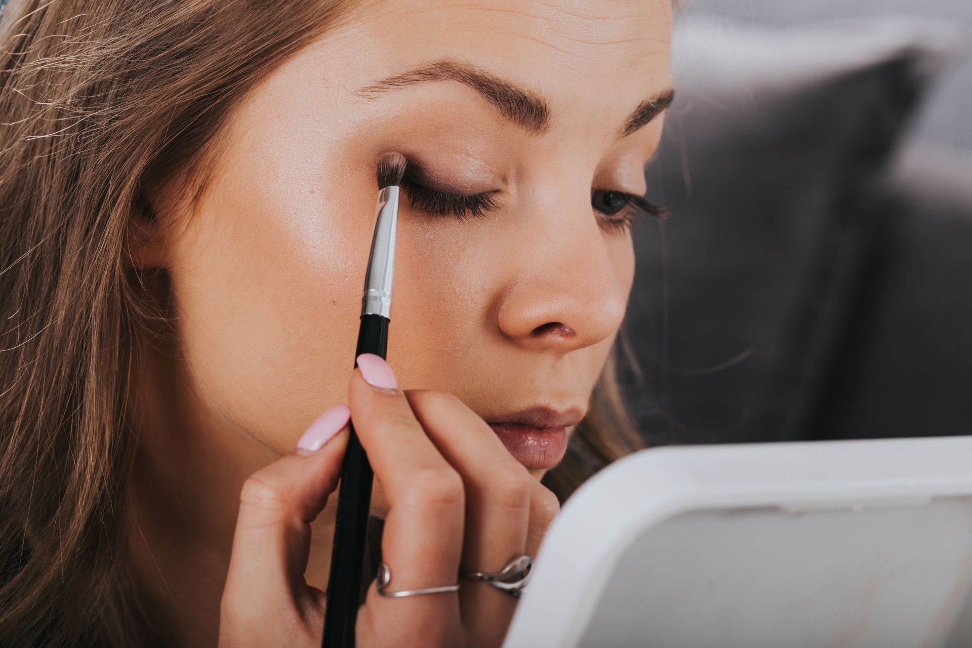 Woman applying eyeshadow with a brush, looking in a mirror.