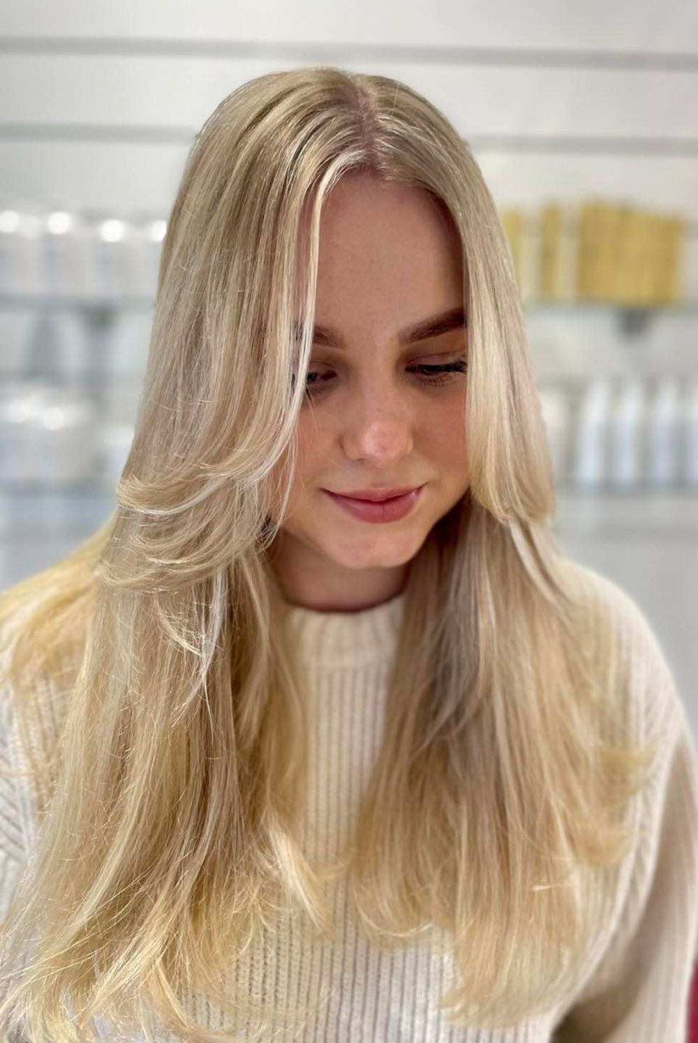 Blonde Woman With Layered Hair Smiles in a Salon, Wearing a Cream Sweater — Strut Hair & Beauty In Maroochydore, QLD