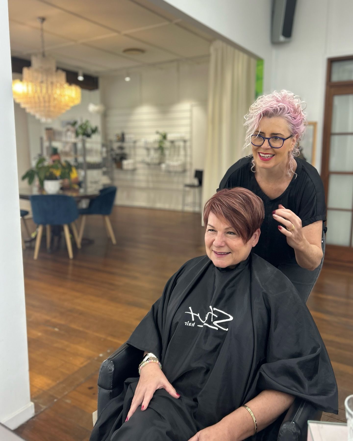A Man is Sitting in a Chair in a Hair Salon While a Woman Stands Behind Him — Strut Hair & Beauty In Maroochydore, QLD