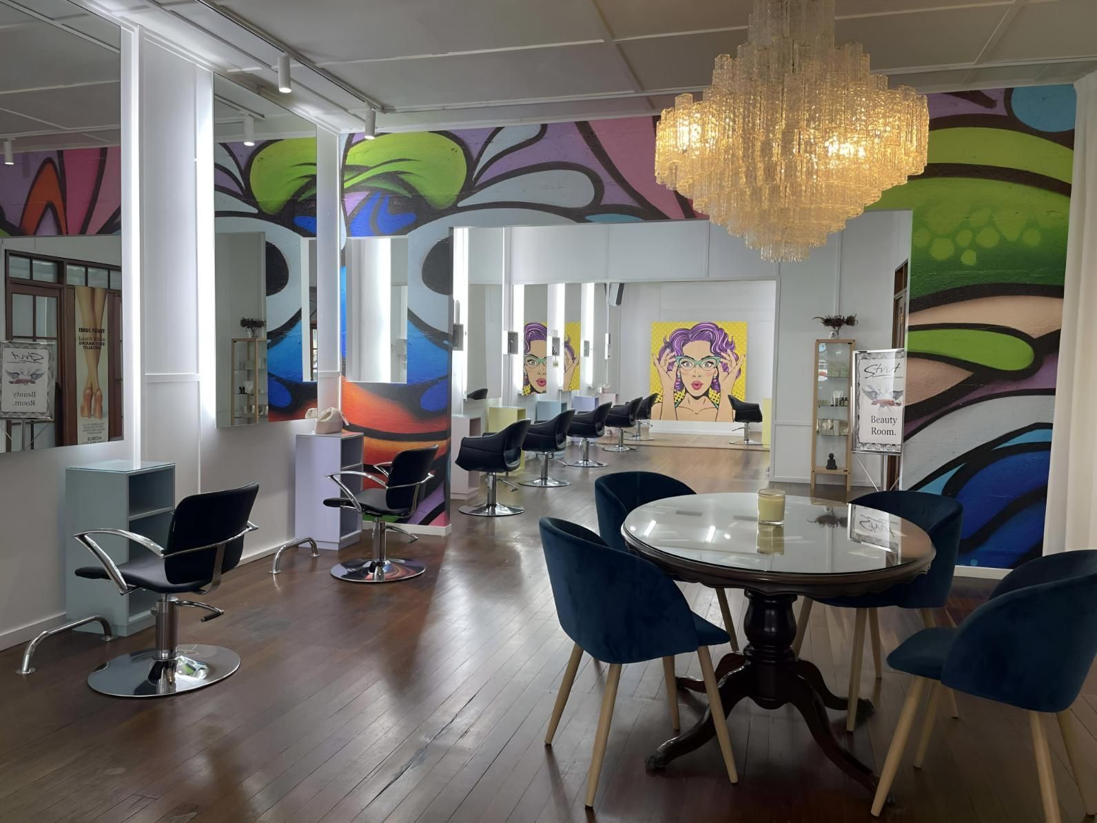A Salon With a Table and Chairs and a Chandelier Hanging From the Ceiling — Strut Hair & Beauty In Maroochydore, QLD