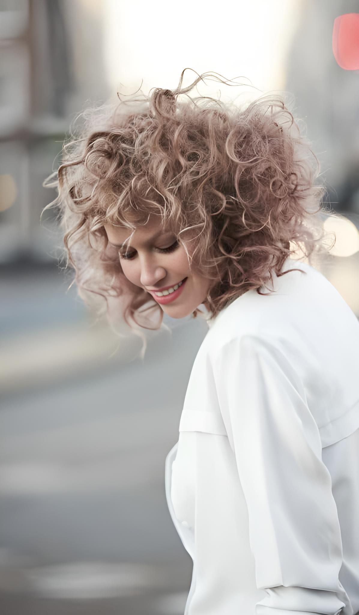 A Woman With Curly Hair is Wearing a White Shirt and Smiling — Strut Hair & Beauty In Maroochydore, QLD