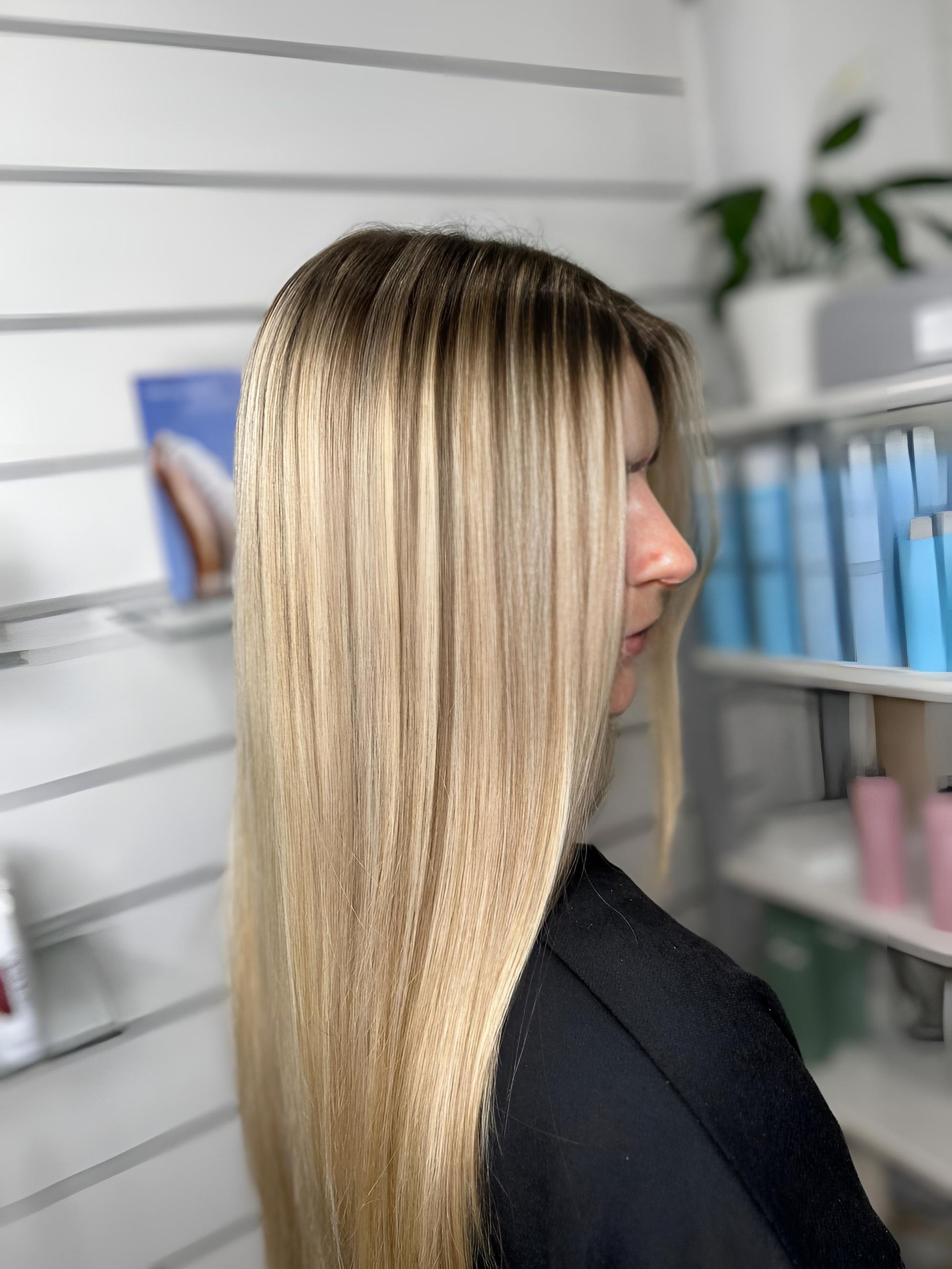 A Woman is Standing in Front of a Shelf of Hair Products— Strut Hair & Beauty In Maroochydore, QLD