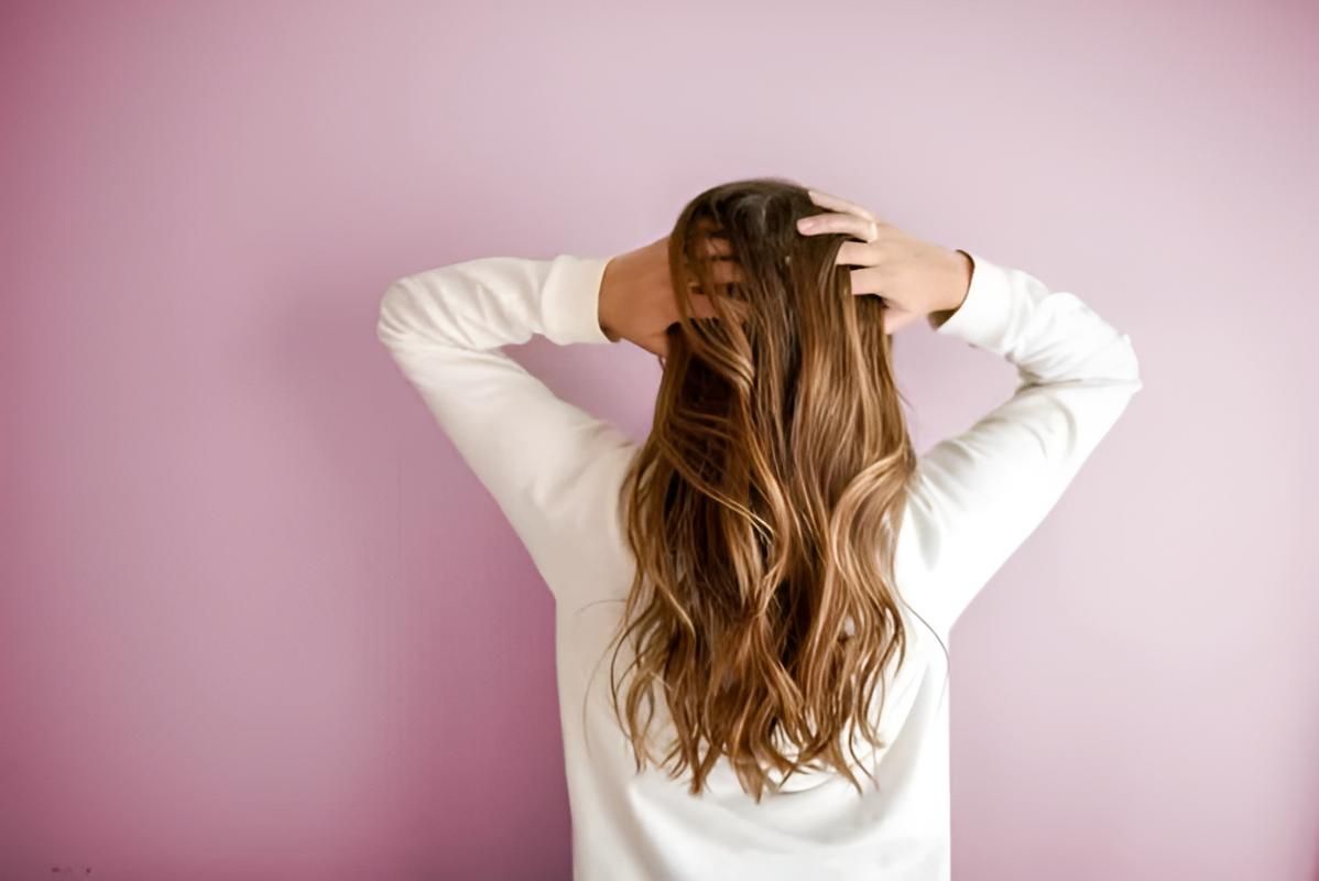 A Woman is Holding Her Hair in Front of a Pink Wall — Strut Hair & Beauty In Maroochydore, QLD