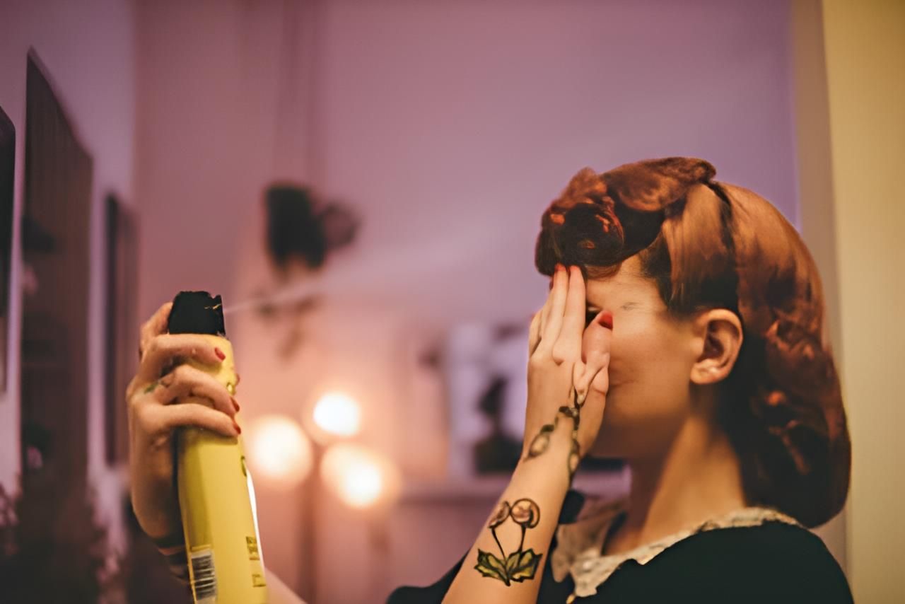 A Woman is Spraying Her Hair in Front of a Mirror — Strut Hair & Beauty In Maroochydore, QLD
