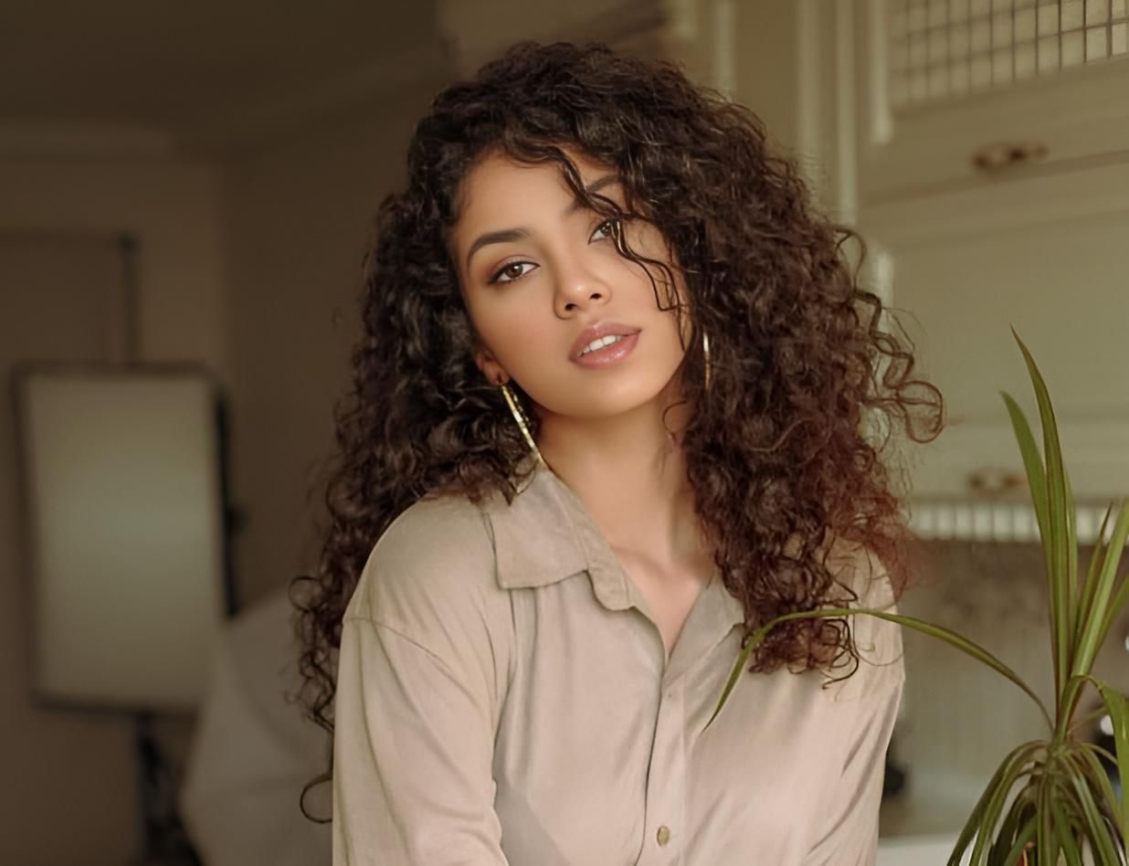 A Woman With Curly Hair is Standing Next to a Plant in a Kitchen — Strut Hair & Beauty In Maroochydore, QLD