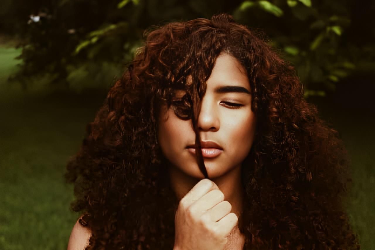 A Woman With Curly Hair is Holding Her Hair in Front of Her Face — Strut Hair & Beauty In Maroochydore, QLD